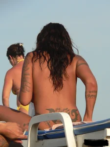 Topless tattooed lady on the beach with fake big tits