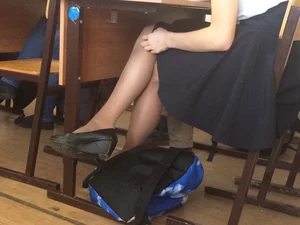 College Girl in a Long Skirt And Pantyhose Touching Her Slim Leg While Sitting at the Desk in the Classroom