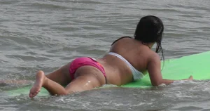 Brunette bikini girl on the beach and surfing in her bikini