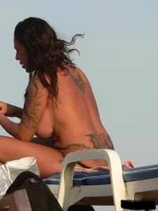 Topless tattooed lady on the beach with fake big tits