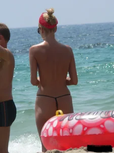 Topless skinny blonde lady in a g-string bikini at the beach
