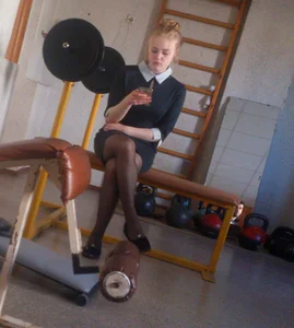 Girl in a Dress and Black Pantyhose Sitting in the College Gymnasium with Her Phote