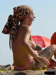 Topless tattooed lady at the beach with a nice ass in pink thong bikini