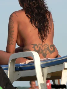 Topless tattooed lady on the beach with fake big tits