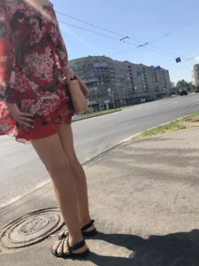Hot street candid girl wearing a short dress and sandals standing on the crosswalk, wind is playing with her hair