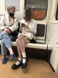 Adorable Young Girl in a Face Mask And White Lace Ruffle Socks Sitting in a Subway Train With Crossed Legs