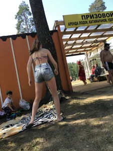 Young Skinny Girl Taking Off Her Denim Shorts Leaving a Swimsuit - Bending Over While Laying a Blanket on the Ground at a Lake Nature Park Gallery