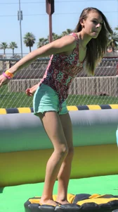 Brunette skinny teen in green shorts playing in a bounce house
