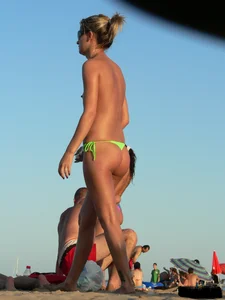 Topless girl on the beach with small boobs wearing a green thong bikini