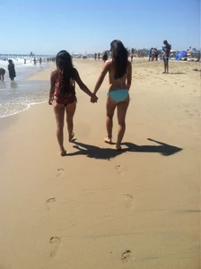 Two Girls in Swimsuits Walking on a Beach Holding Hands Creepshot
