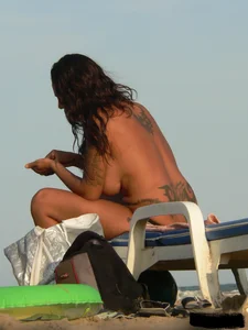Topless tattooed lady on the beach with fake big tits