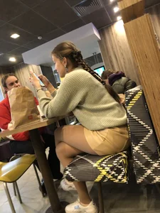 Cute teen in a short skirt and pantyhose sitting with crossed legs in a fast food restaurant creepshot