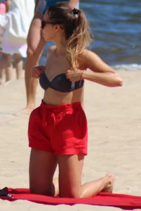 Hottie undressing from her red shorts to her bikini to layout on the beach