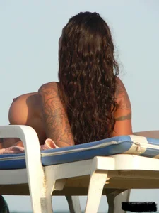 Topless tattooed lady on the beach with fake big tits