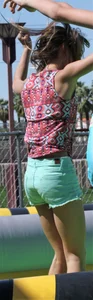Brunette skinny teen in green shorts playing in a bounce house