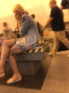 Candid girl in a skirt and sandals sitting with crossed legs at the subway station
