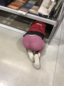 Girl in leggings on her knees crawling under the shelf at the book store creepshot