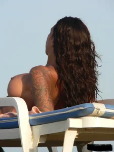 Topless tattooed lady on the beach with fake big tits