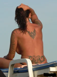 Topless tattooed lady on the beach with fake big tits