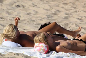 Topless mom and daughter on the beach getting some sun