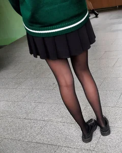 Cute young girl in a skirt and black pantyhose sitting on the floor with her shoes off