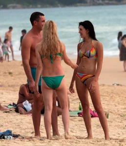 Sexy brunette in thong bikini and blonde friend in green bikini at the beach