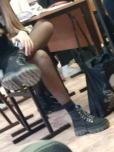 Candid teen college girl wearing boots and black pantyhose sitting with crossed legs at her desk in class, very skinny legs