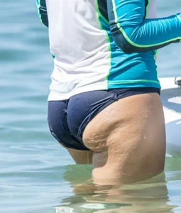 Girl in the water in a navy blue bikini bottom, shirt and hat with a nice ass