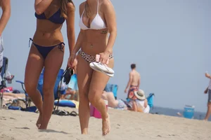 Two sexy friends, one blonde and one brunette, on the beach in bikinis
