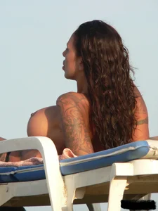 Topless tattooed lady on the beach with fake big tits