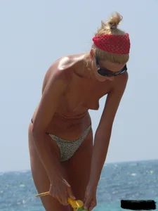 Topless skinny blonde lady in a g-string bikini at the beach