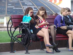Bunch of young girls sitting on a park bench on the street with crossed legs, wearing pantyhose and short dresses