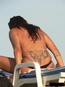 Topless tattooed lady on the beach with fake big tits