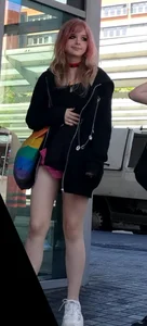 Awesome teen girl with pink dyed hair in hosrts sitting on the ground at the bus stop