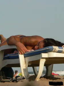 Topless tattooed lady on the beach with fake big tits