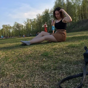 Girl in a Skirt and Socks Sitting on the Grass at the Forest Clearing