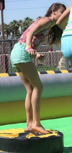 Brunette skinny teen in green shorts playing in a bounce house