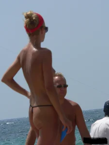 Topless skinny blonde lady in a g-string bikini at the beach