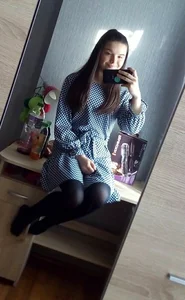 Cute Girl in a Polka-Dot Dress And Black Pantyhose on Her Thin Legs Sitting on a Desk Mirror Selfie