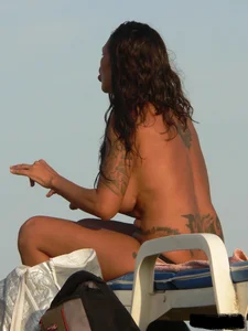 Topless tattooed lady on the beach with fake big tits