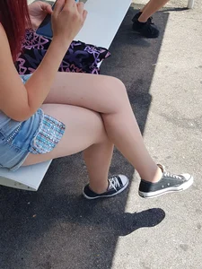 Young candid girl in jean shorts sitting at the bus stop with crossed legs creepshot