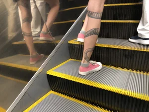 Girl in a Skirt With a Snake Tattoo on Her Leg Standing With Spread Legs on an Escalator Creepshots Series