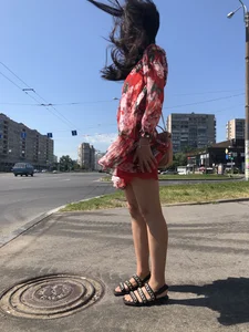 Hot street candid girl wearing a short dress and sandals standing on the crosswalk, wind is playing with her hair