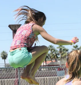 Brunette skinny teen in green shorts playing in a bounce house