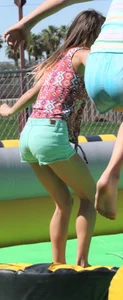 Brunette skinny teen in green shorts playing in a bounce house