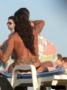 Topless tattooed lady on the beach with fake big tits