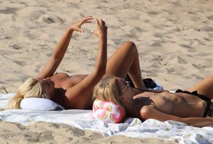 Topless mom and daughter on the beach getting some sun