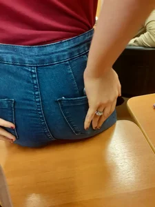College candid teen wearing tight blue jeans sitting on desk and placing hand on her booty closeup photo