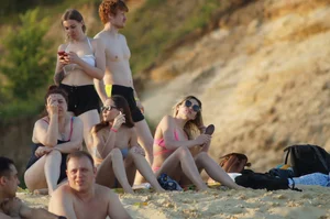 Group of Girls in Swimsuits Sitting on the Sand on the Beach Creepshot