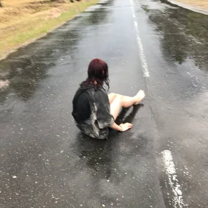 Teen with red wet hair lying on asphalt, wet after rain